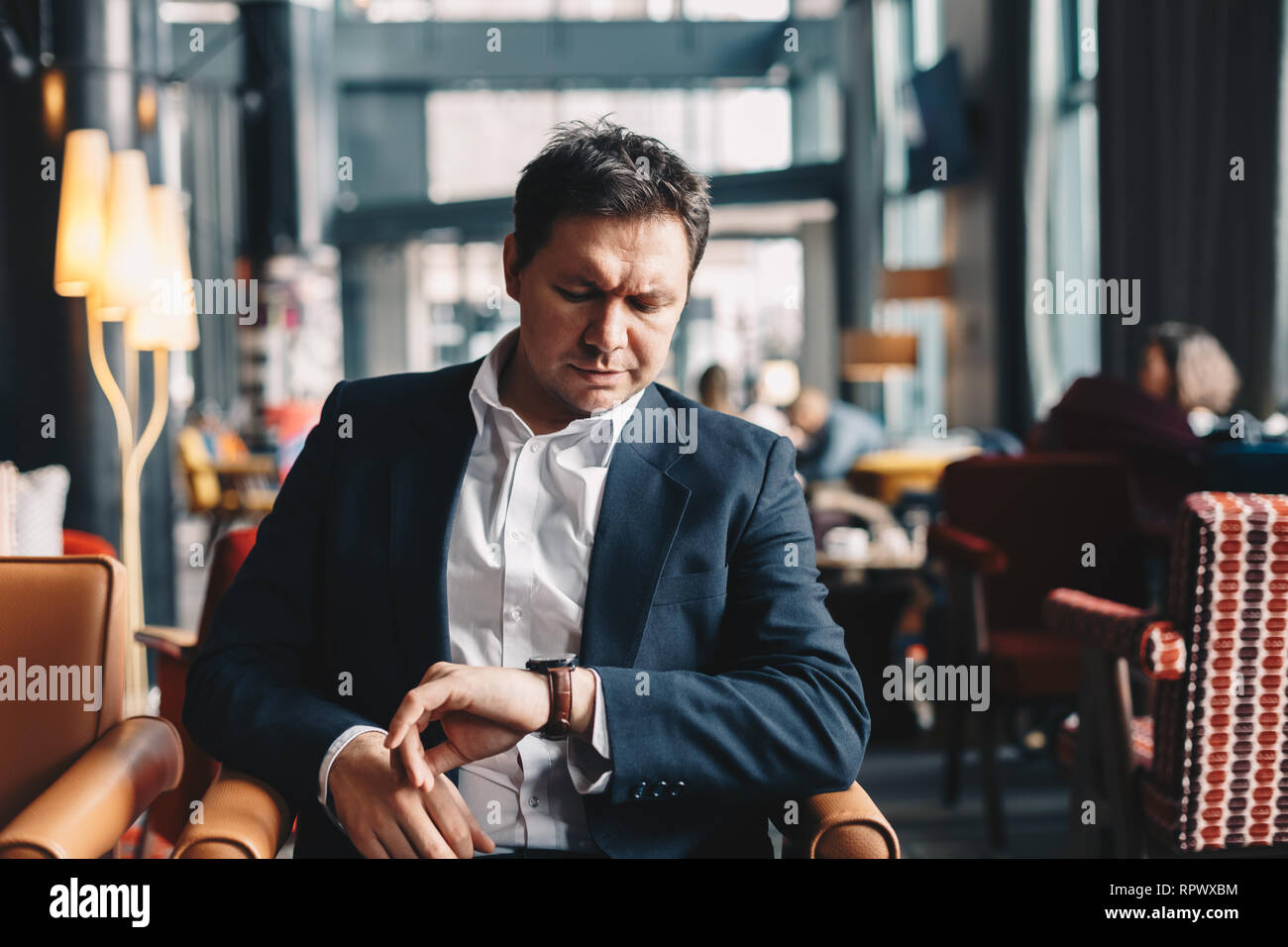 In der Nähe der gut aussehende junge Mann sitzt in einem Café Bar, mit Blick auf seine Hand beobachten, wie er darauf warten, dass jemand kommt und eine geschäftliche Besprechung haben Stockfoto