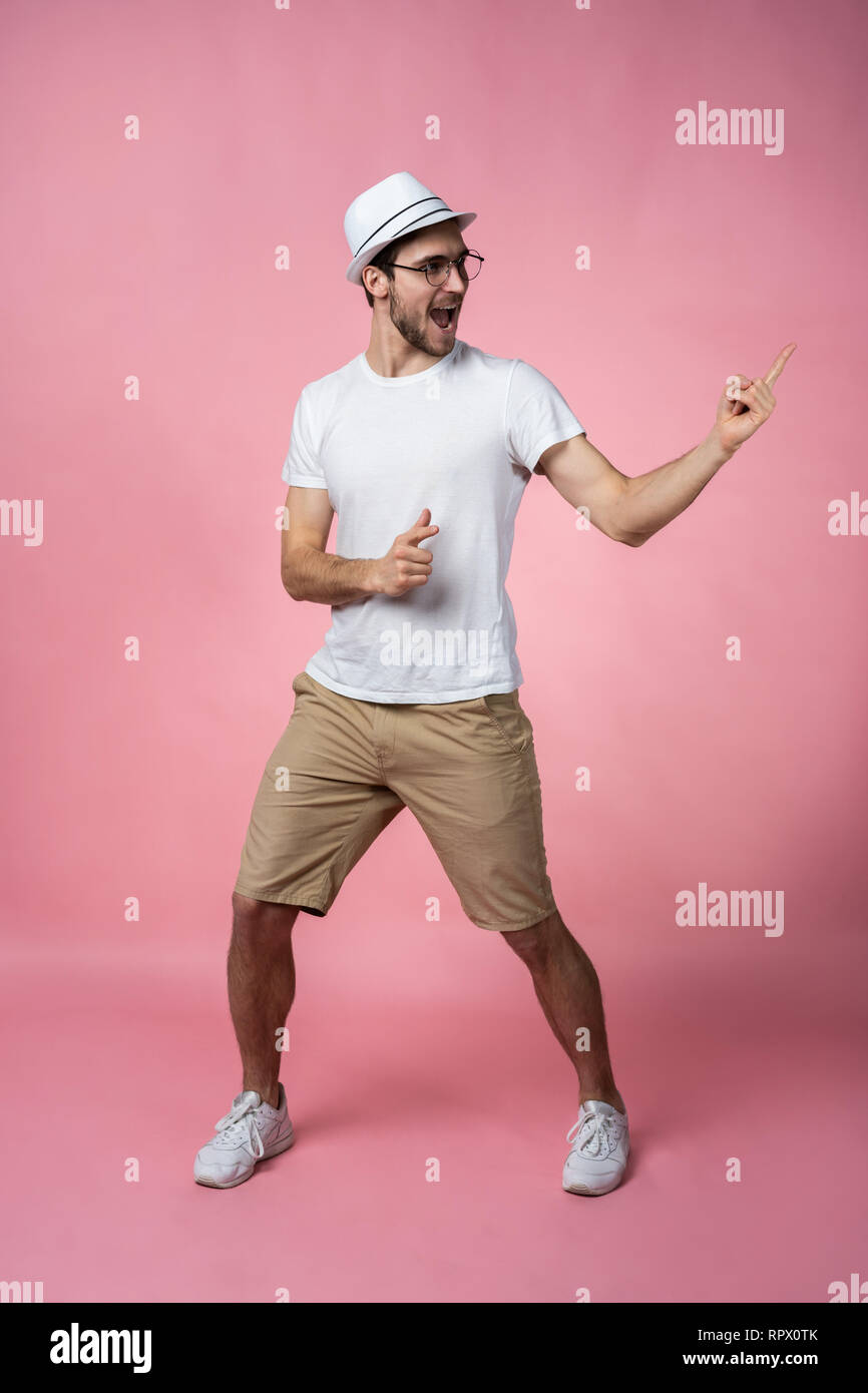 Attraktive lächelnden jungen Mann arm Finger zeigen zu leeren Raum in nur haben signal legere weißes T-Shirt auf rosa Hintergrund isoliert. Stockfoto