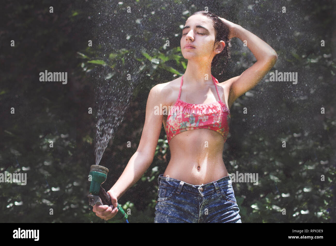 Stehendes Mädchen im Garten an einem heißen Tag mit einem Wasserschlauch Stockfoto