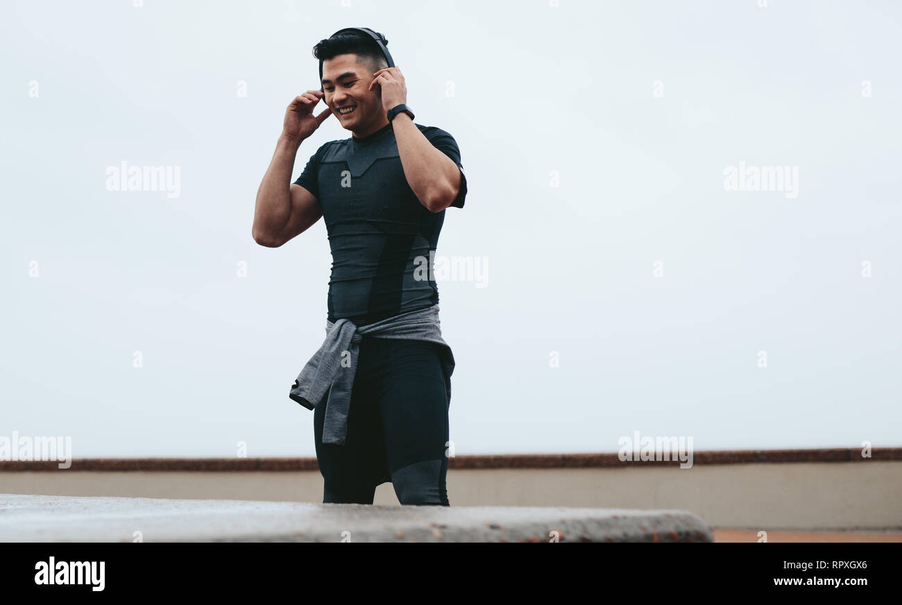 Passen junge asiatischer Mann in Sportkleidung tragen Kopfhörer Musik während outdoor training zu hören. Lächelnd Sportler die Pause vom Training und von Symbol Stockfoto