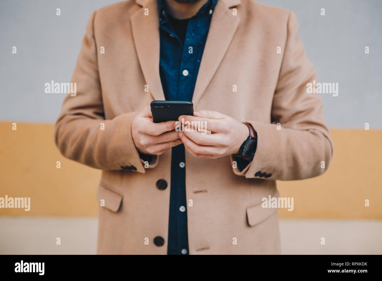 Nahaufnahme Detail shot von modischen Jungen mit seinem Handy Mann mit Chesterfield Herren Mantel in Kamel Farbe, vor einem bunten b Stockfoto