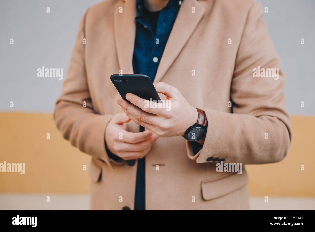Close-up Detail shot von modischen jungen Mann mit seinem Handy, das Tragen von Chesterfield von Herren Mantel in der Farbe gelb, vor einem bunten zurück Stockfoto