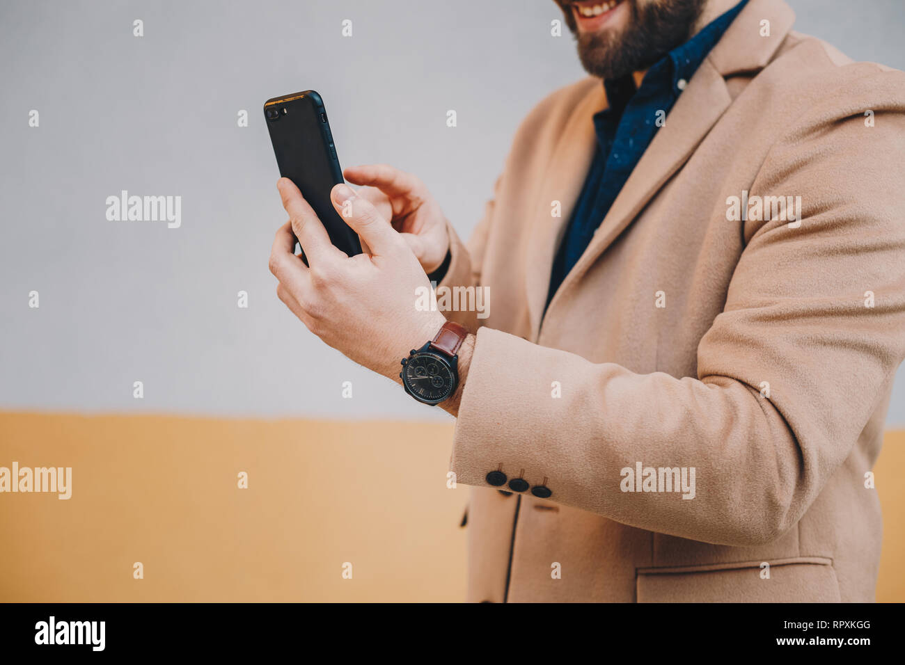 Nahaufnahme Detail shot von modischen, junge Bartgeier über sein Handy Mann mit Camel chesterfield Herren Mantel vor einem bunten Ba Stockfoto