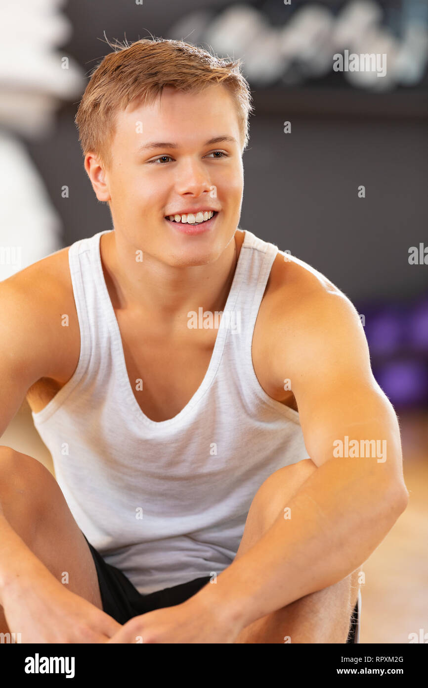 Lächelnden jungen Mann in workout Outfit auf dem Boden sitzend bei Fitness Gym Stockfoto