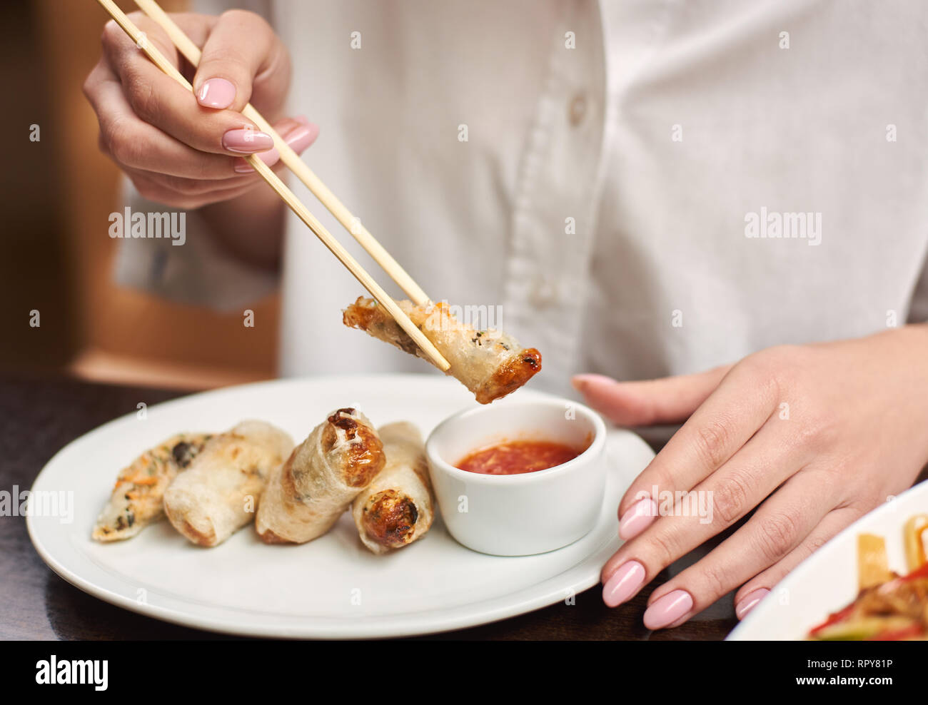 Croped der Frau in weißer Bluse mit Abendessen im Restaurant. Weibliche Hände Maniküre holding Tempura mit Garnelen mit futtersticks. 3-Gänge Mittagessen Stockfoto