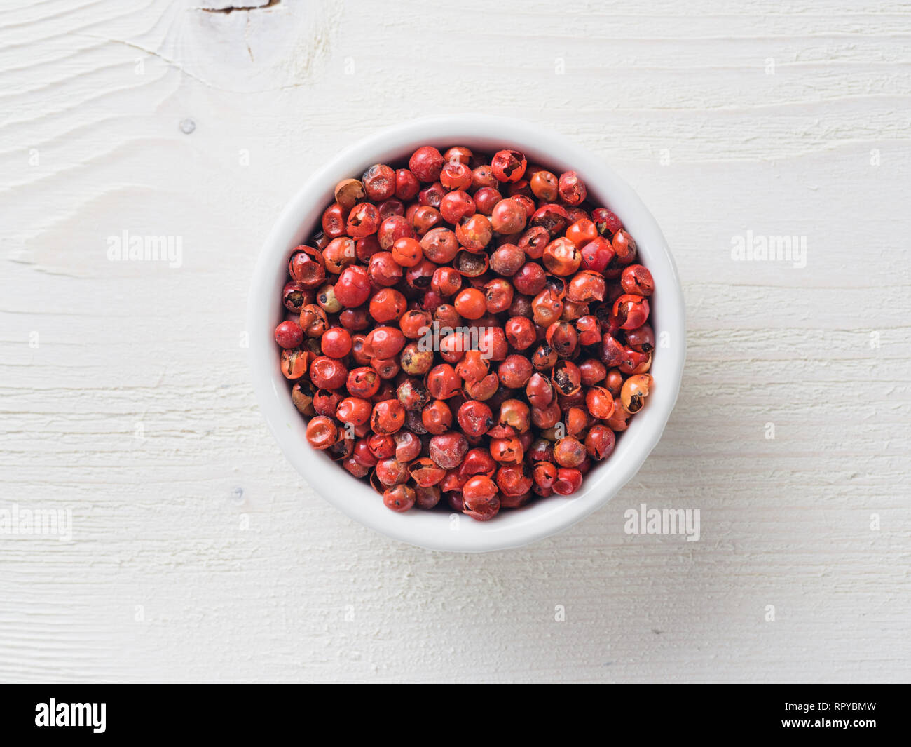 Stapel mit getrockneten Pfeffer rosa Beeren auf weiße Holztisch. Nahaufnahme von rosa Pfeffer. Ansicht von oben oder flach-legen. Stockfoto