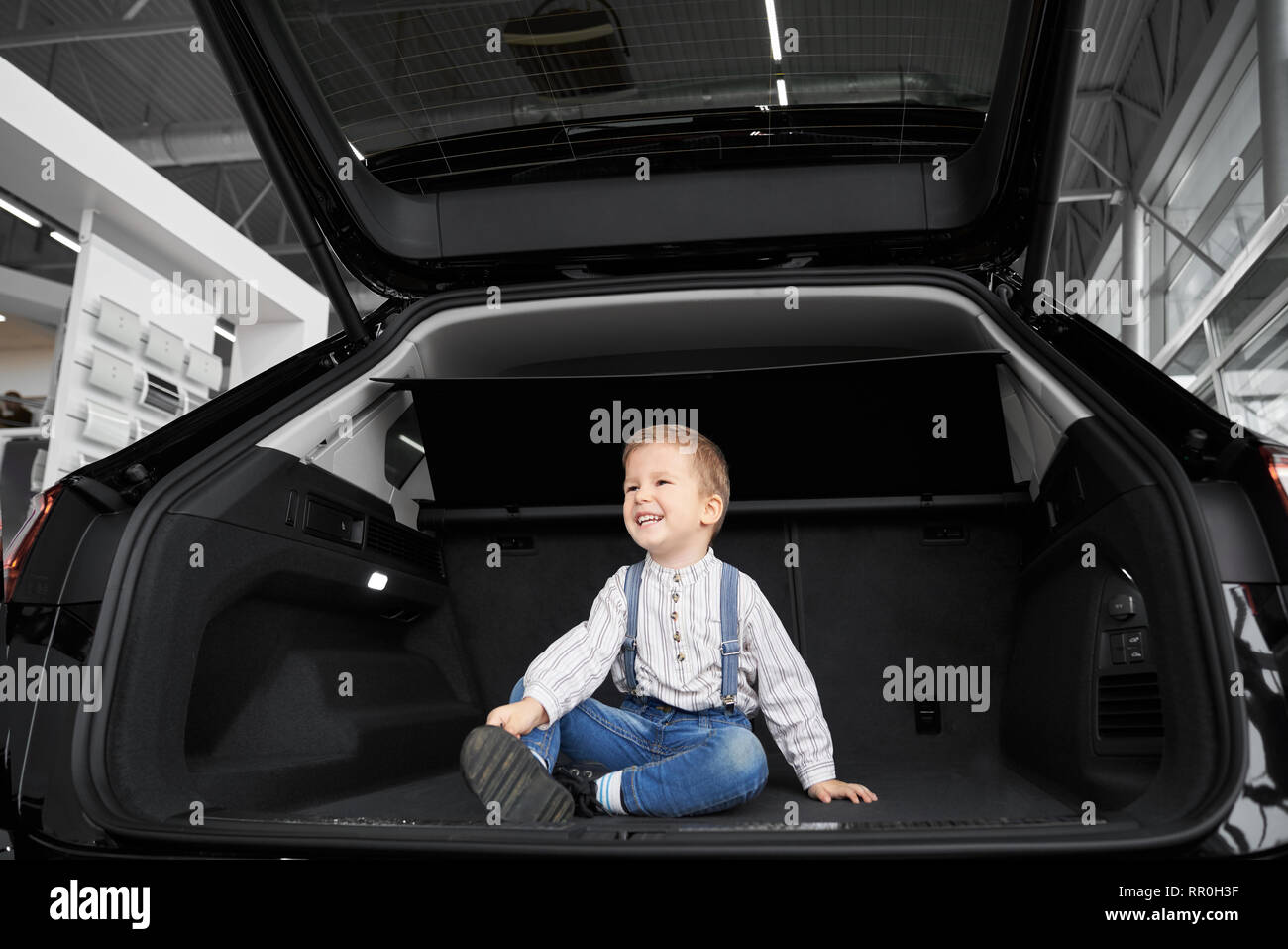 Schön, süße kleine Junge sitzt im Kofferraum von großen, neuen schwarzen Automobils. Hübsches Kind posiert, weg schauen und lächeln. Glückliches Kind beobachten Fahrzeug im Kofferraum. Stockfoto