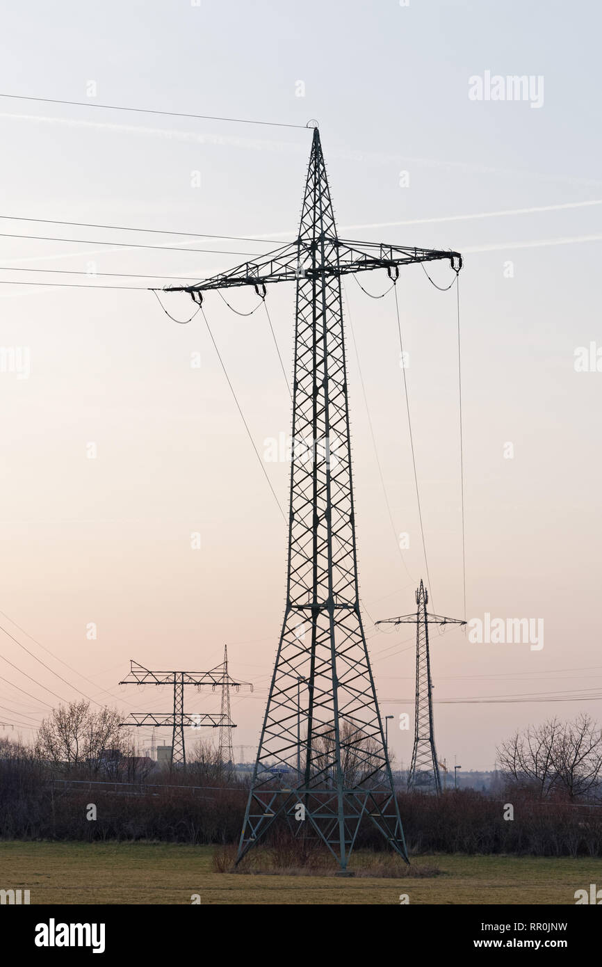 Mehrere große Strommasten in verschiedene Typen mit Kabel, Sie werden gestaffelt als Silhouetten vor einem leicht gefärbten Abendhimmel mit Con Stockfoto