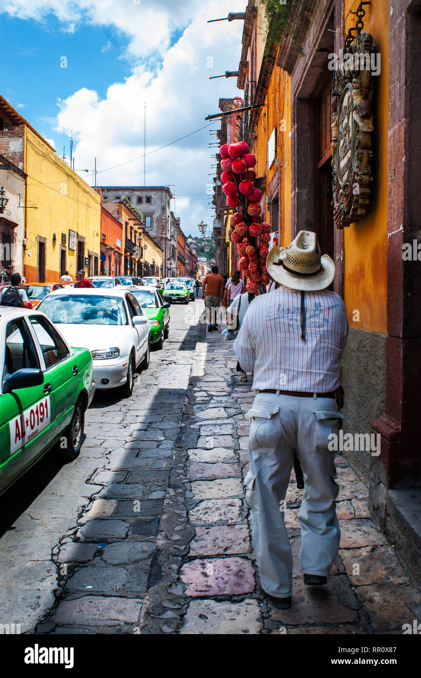 Mexiko, San Miguel de Allende belebten Straße Szene mit Candy Apple Verkäufer gehen auf die Straße mit Kopfsteinpflaster. Die malerische Stadt ist ein beliebtes Ziel. Stockfoto