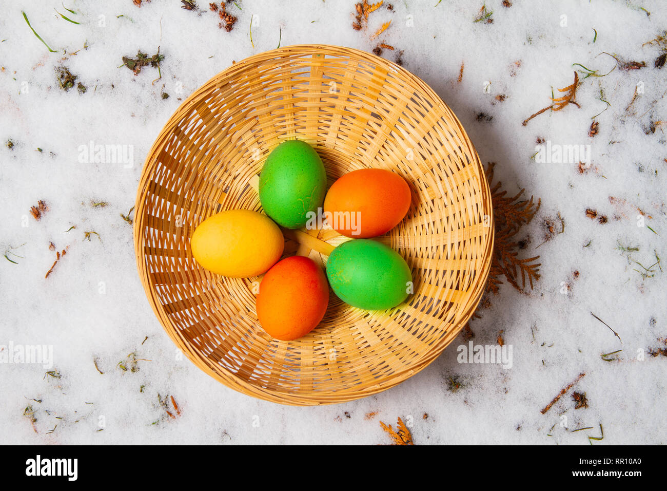 Fünf bunte Ostereier in einem Strohkorb auf Schnee und Gras isoliert Ostereiersuche Stockfoto