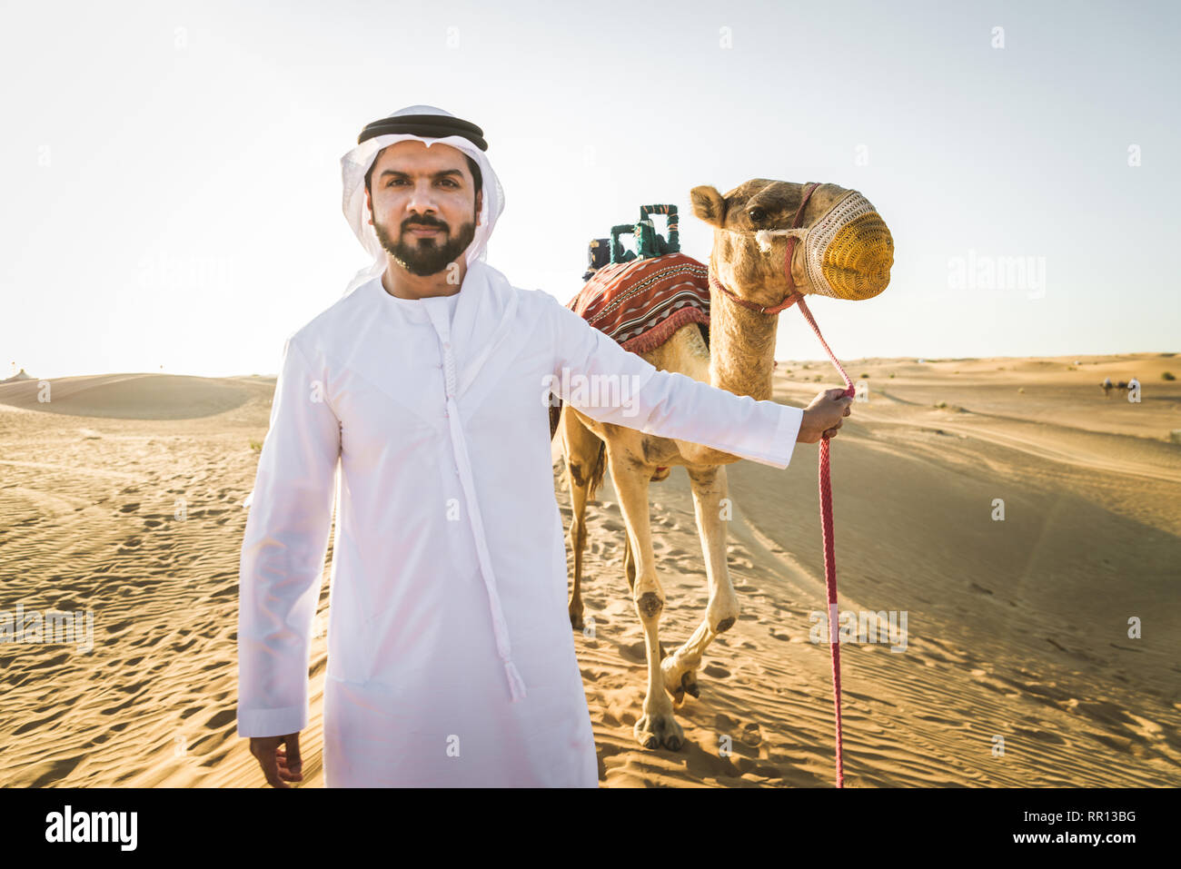 Stattlich im Nahen und Mittleren Osten Mann mit kandura und gatra reiten auf einem Kamel in der Wüste Stockfoto