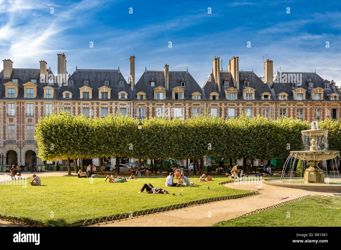 Menschen sitzen und sonnen sich auf den Rasenflächen am Place des Vosges im schicken Viertel Le Marais in Paris, Frankreich Stockfoto
