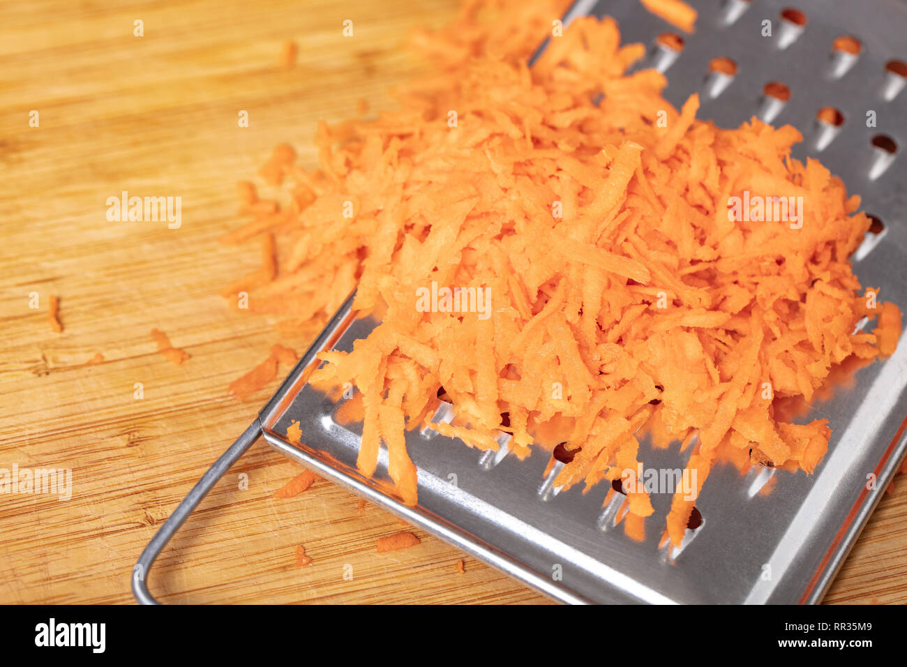 Zerfetztes Karotten auf dem Reibeisen closeup, Holz- Hintergrund Stockfoto