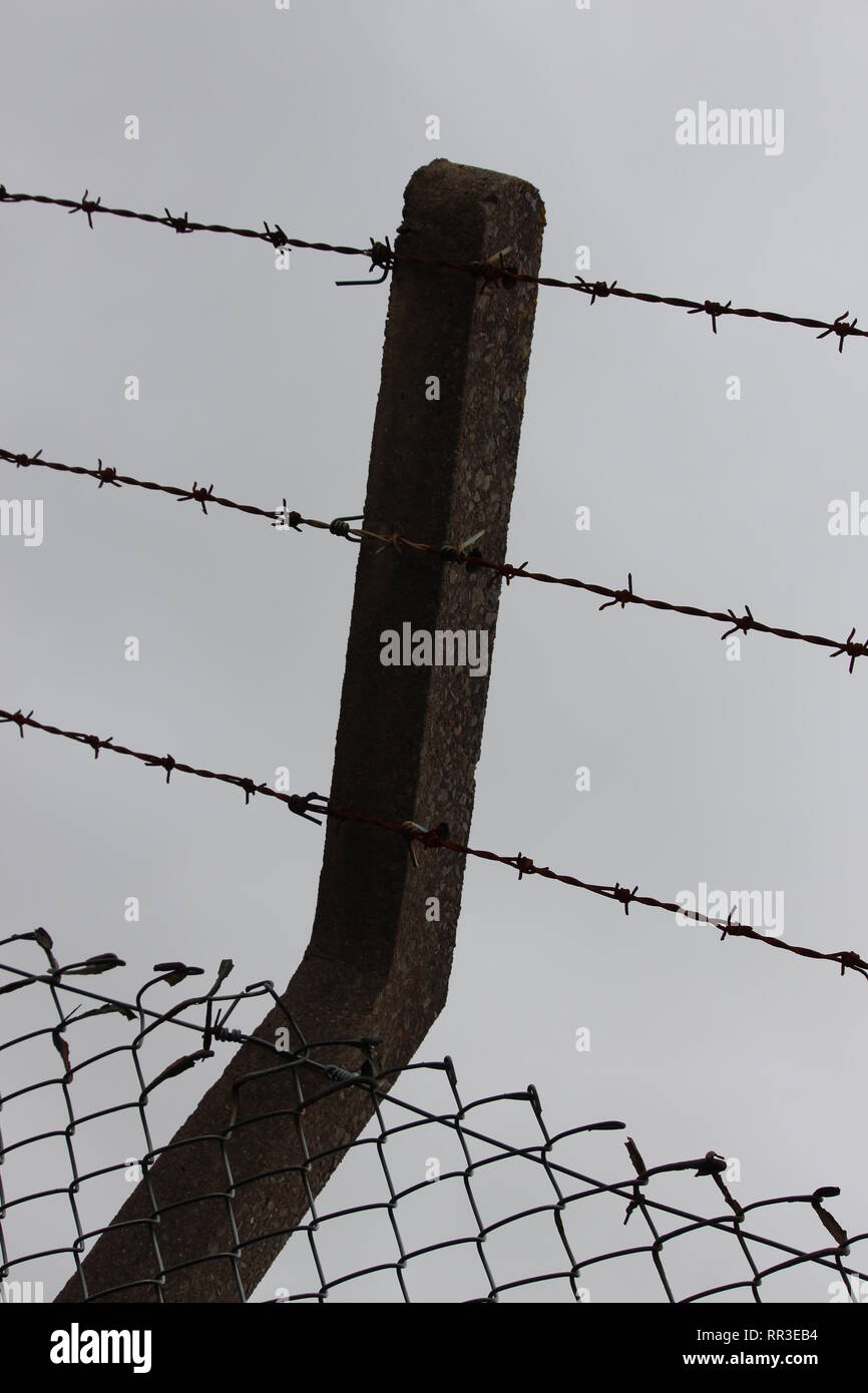 Eine Nahaufnahme Foto von Sicherheit Fechten, zu Stacheldraht und Chain link Fencing, auf einen konkreten Beitrag. Sicherheit, Grenze, Sicherheitskonzept Stockfoto