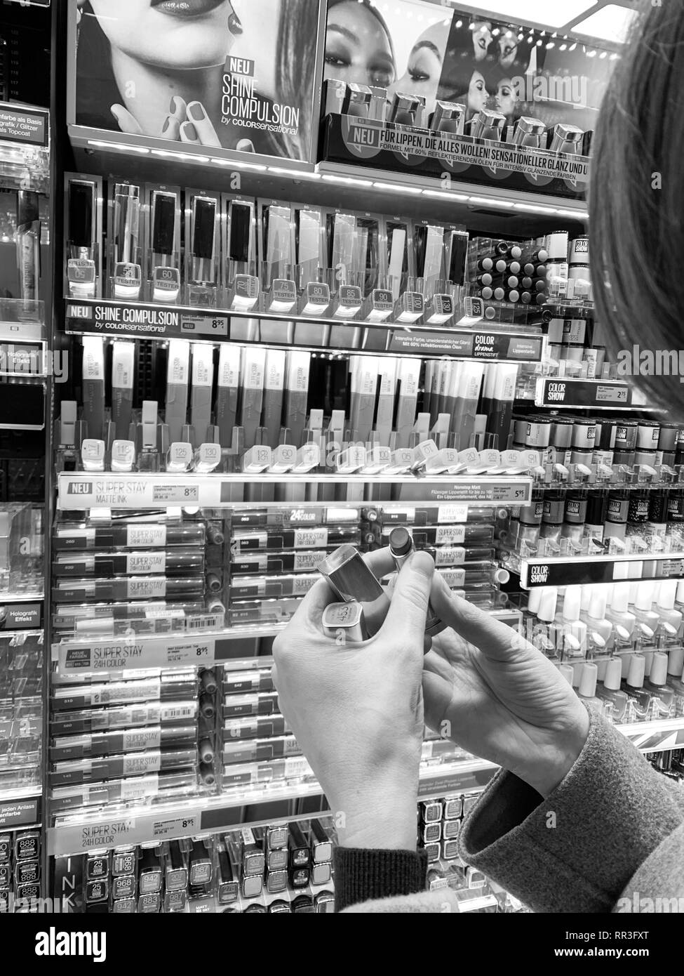 München, Deutschland - 27.Oktober 2018: die Frau in der Kosmetik kaufen Red store Lippenstift liner zeichenstift zwischen der Vielzahl Auswahl aus verschiedenen Marken - Prüfung Farbe auf der Rückseite der Hand Schwarz und Weiß Stockfoto