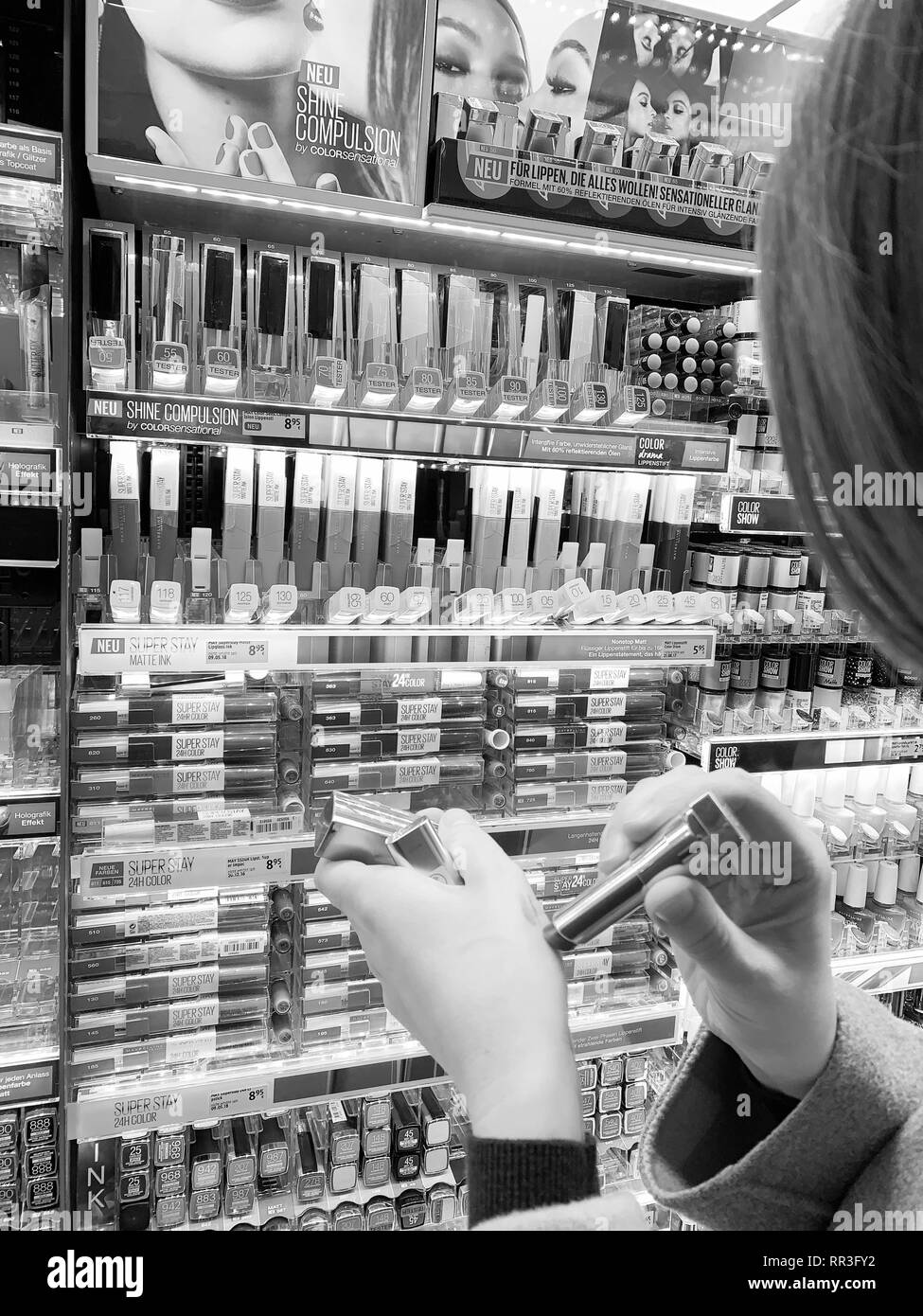München, Deutschland - 27.Oktober 2018: die Frau in der Kosmetik kaufen Red store Lippenstift liner zeichenstift zwischen der Vielzahl Auswahl aus verschiedenen Marken - Prüfung Farbe auf der Rückseite der Hand Schwarz und Weiß Stockfoto