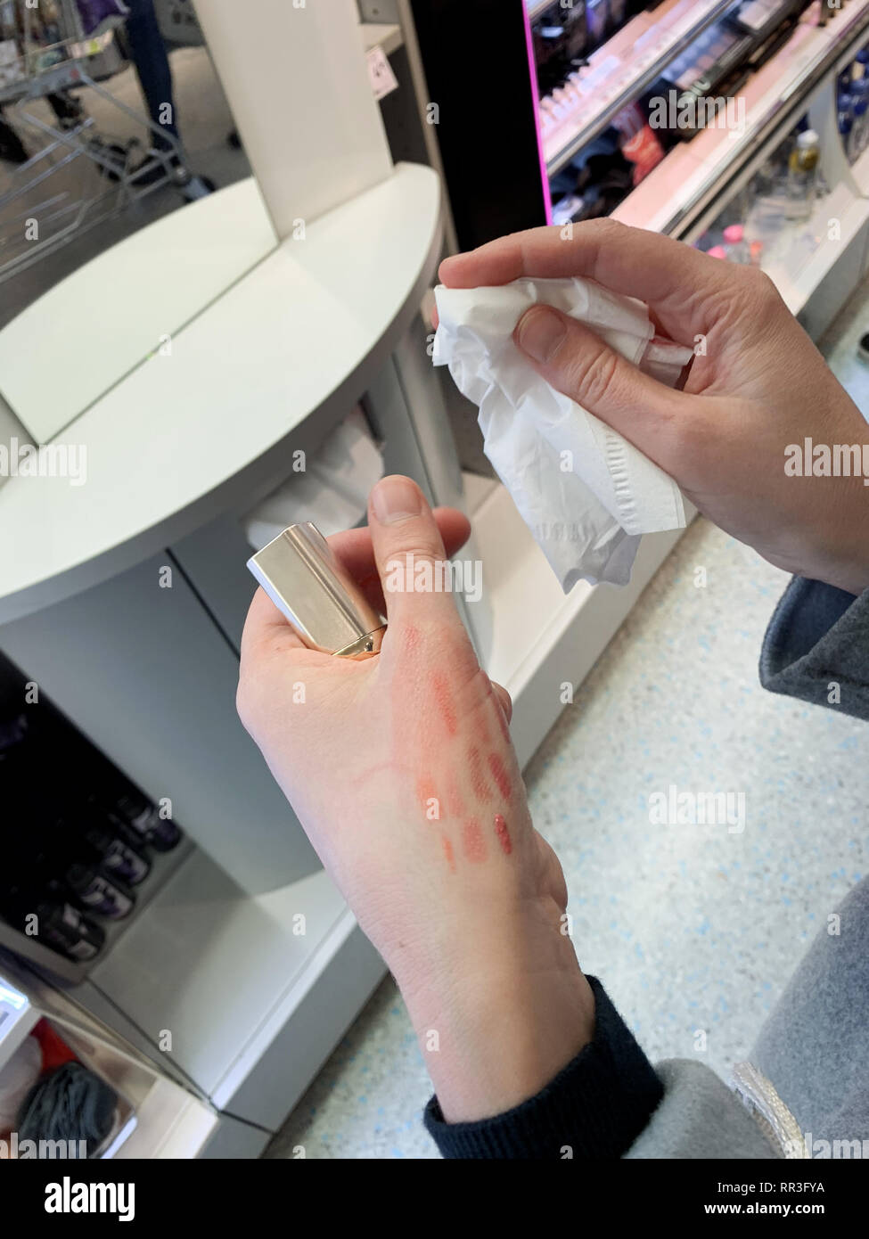 Deutsche Frau Reinigung roten Lippenstift liner Zeichenstift nach der Prüfung Farbe auf der Rückseite der Hand Stockfoto