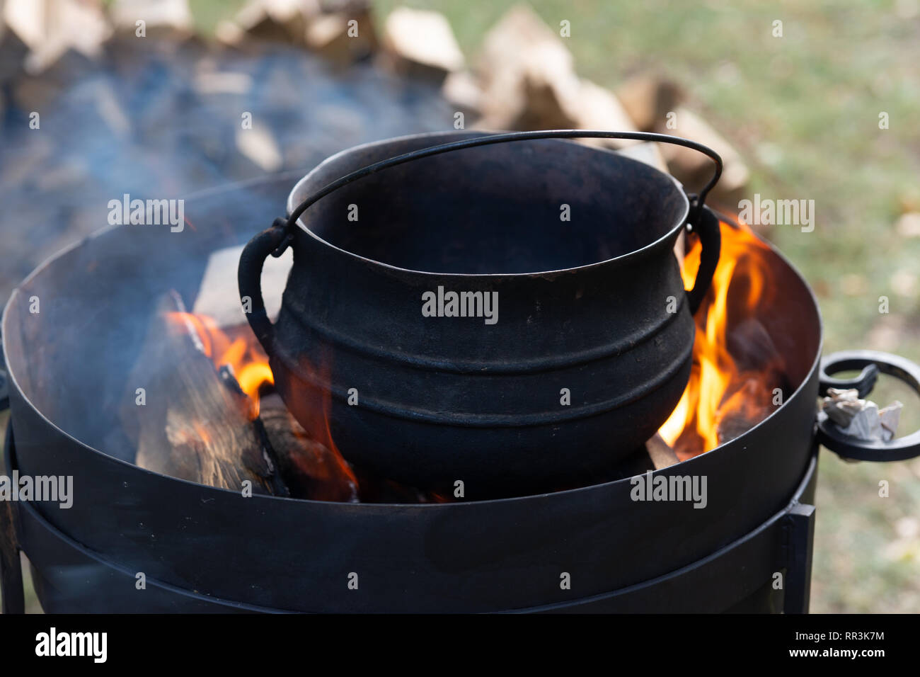 Zubereitung von Essen auf offenem Feuer. Black Metal pot, Feuer und Flammen, Rauch, Stapel von Holz im Hintergrund Stockfoto