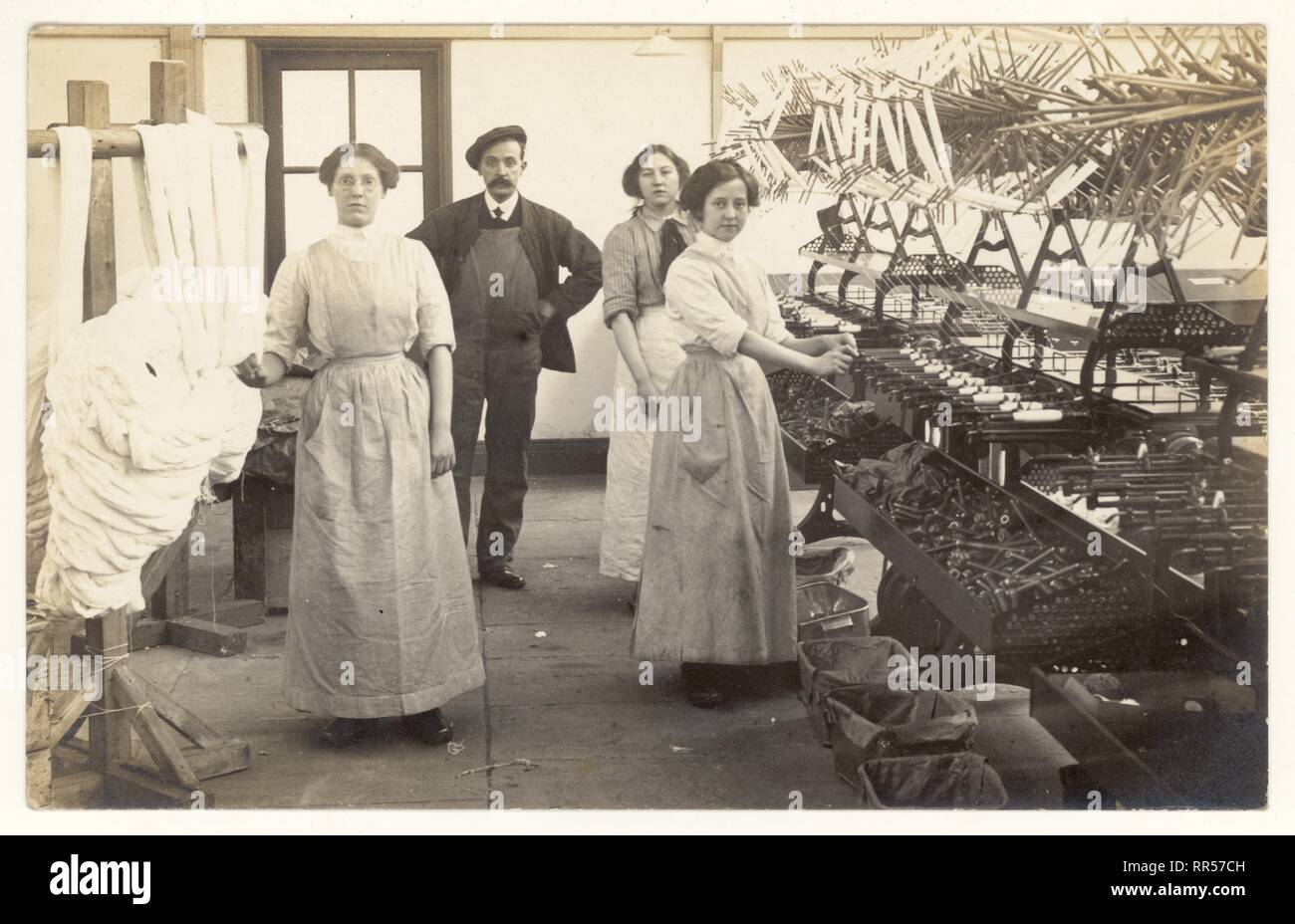 Anfang des 20. Jahrhunderts Originalpostkarte von Bobbin Winder Mädchen und Vorarbeiter, Aufseher oder Arbeiter. Getrocknete Skeins aus Baumwolle aus dem Gestell werden auf den Swift der Wickelmaschine gelegt, die Garn aus dem Skein auf Spulen wickelt, um 1915, Radcliffe, Lancashire, U.K. Stockfoto