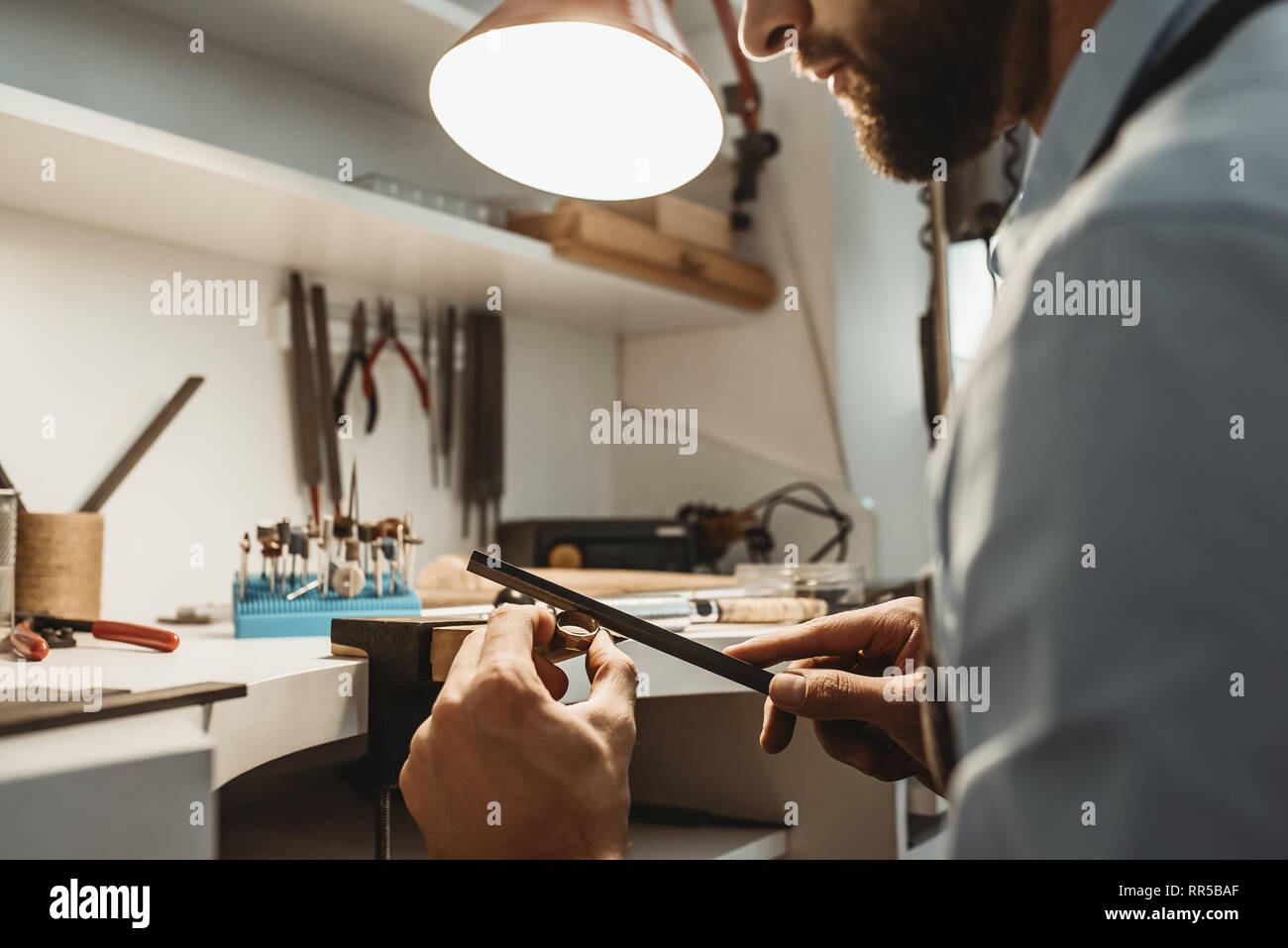 Auf einen Prozess konzentriert. Nahaufnahme eines jungen männlichen Juwelier arbeiten und die Gestaltung eines unfertigen Ring mit einem Werkzeug in der Werkstatt. Schmuck. Busines Stockfoto