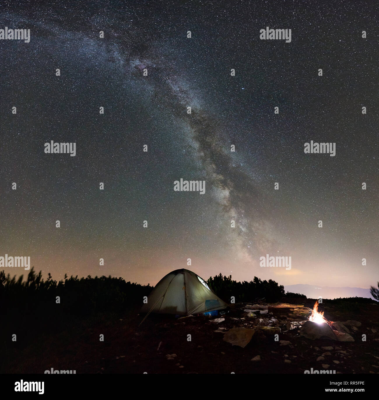 Touristische Campingplatz nachts auf der Oberseite von Rocky Mountain. Leuchtende Zelt und Lagerfeuer unter unglaublich schöne Nacht Himmel voller Sterne und Milchstraße. Auf Hintergrund erstaunliche Sternenhimmel und Berge Stockfoto