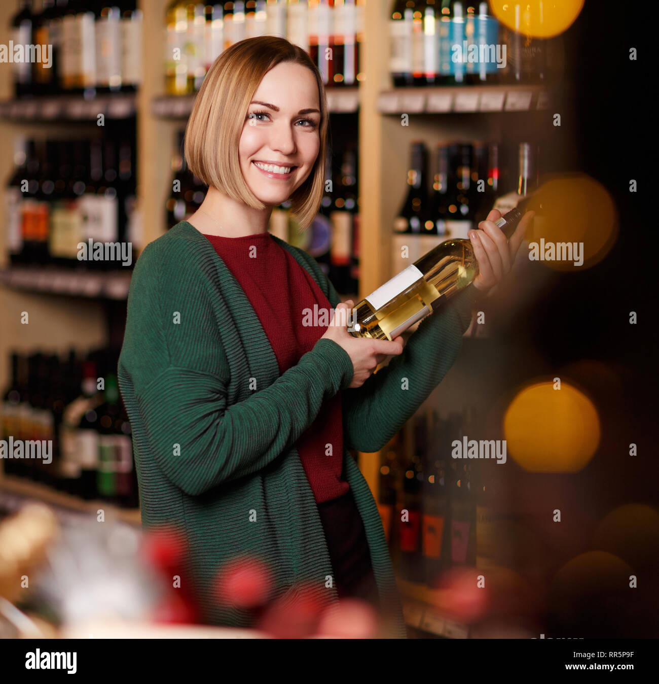 Bild der Frau mit Flasche in der Hand auf unscharfen Hintergrund von Regalen mit Flaschen Wein in Store Stockfoto