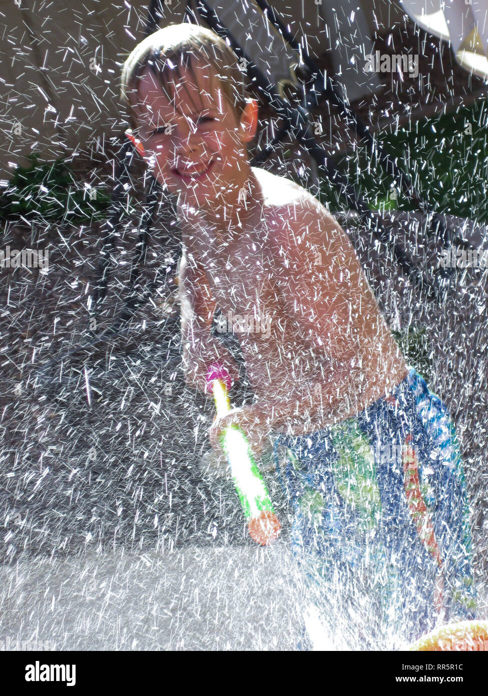 Ein Junge in einem Pool schießt eine hohe angetriebene Squirt gun beim Spielen in einem Pool bei einem Sommertag. Stockfoto