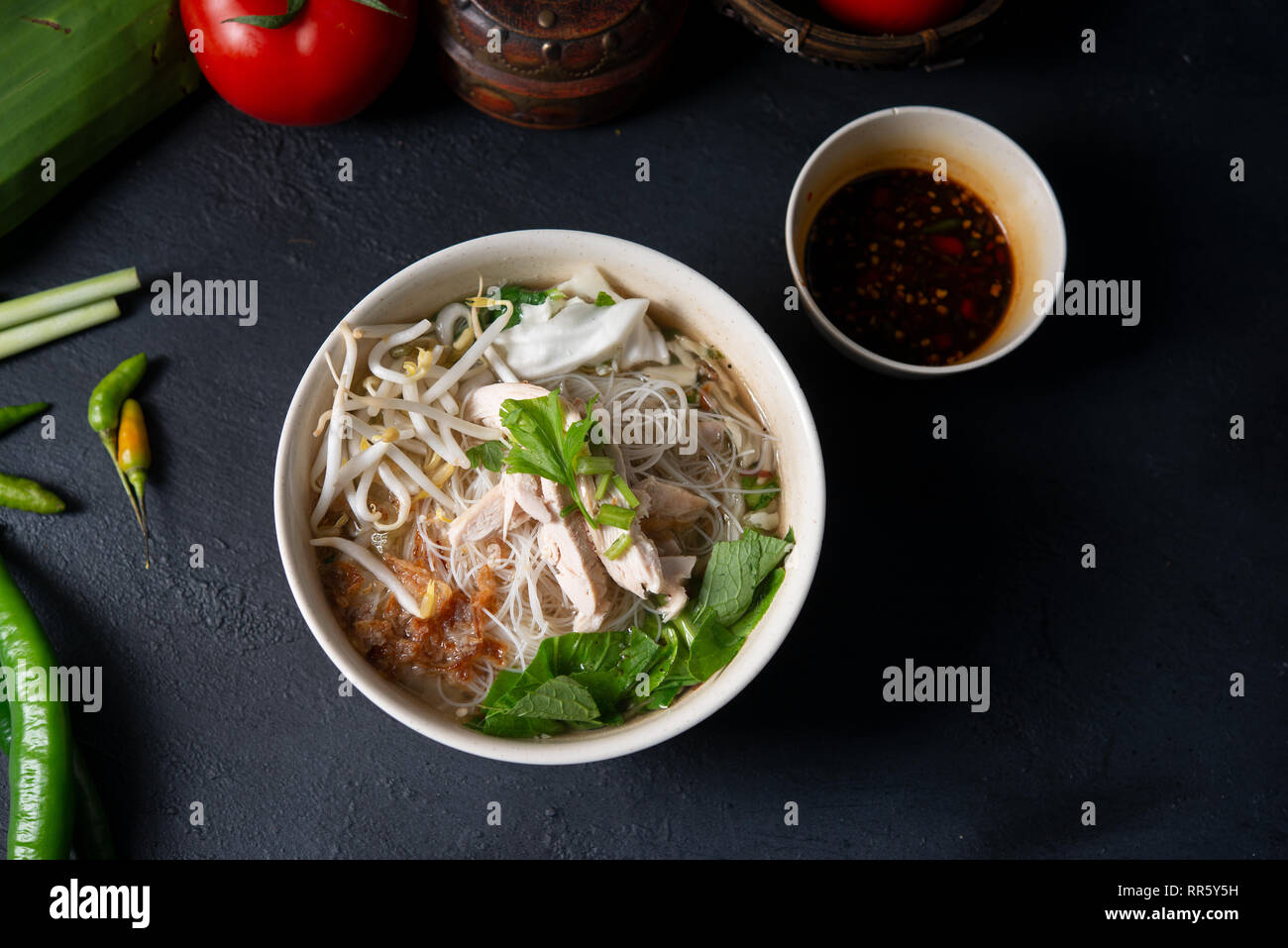 Asiatische Reisnudeln Suppe und Hühnchen in der Schüssel auf dunklem Hintergrund. Ansicht von oben flach. Stockfoto
