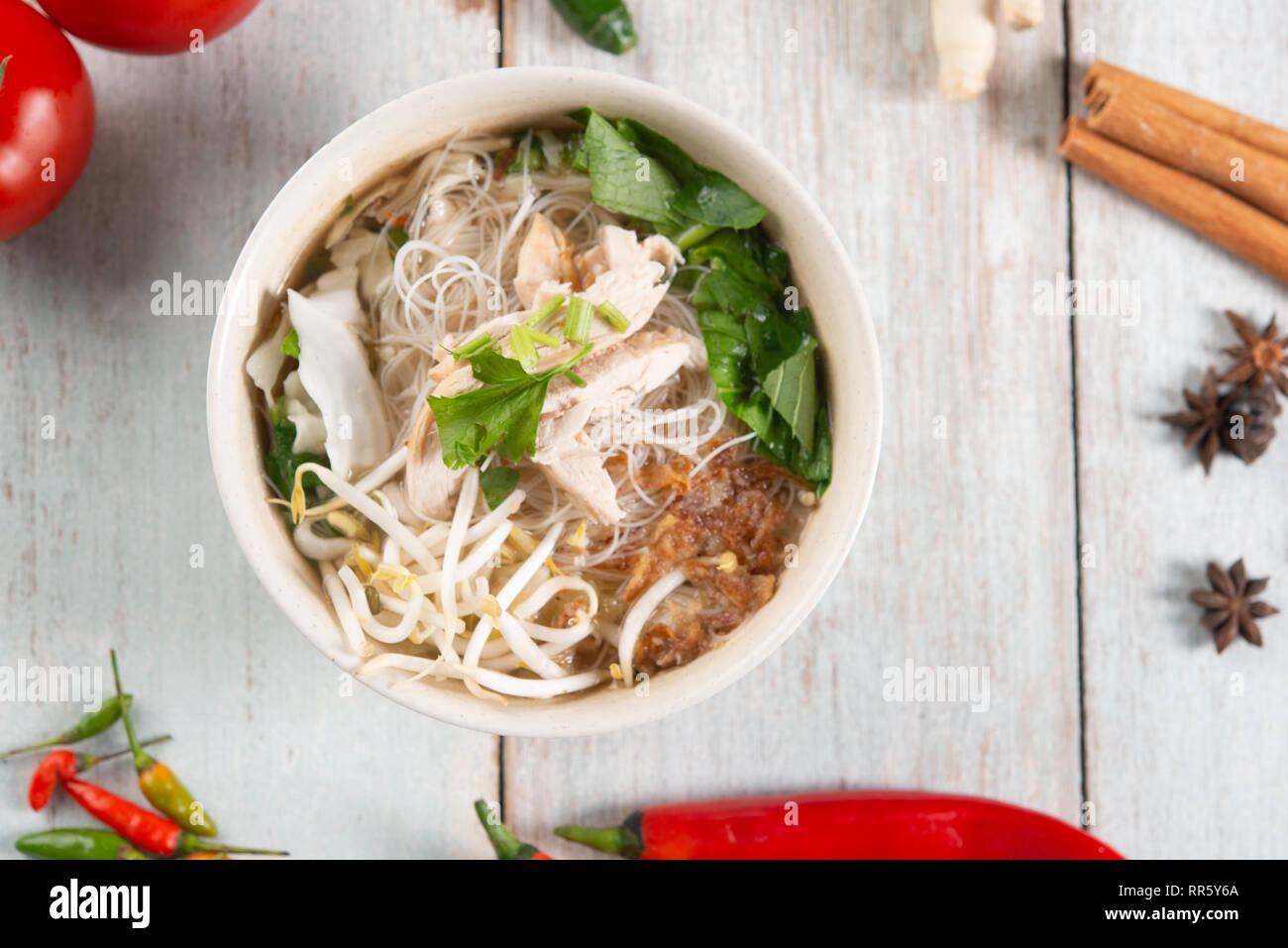 Asiatische Reisnudeln Suppe mit Gemüse und Huhn in der Schüssel. Ansicht von oben flach auf Holz- Hintergrund. Stockfoto