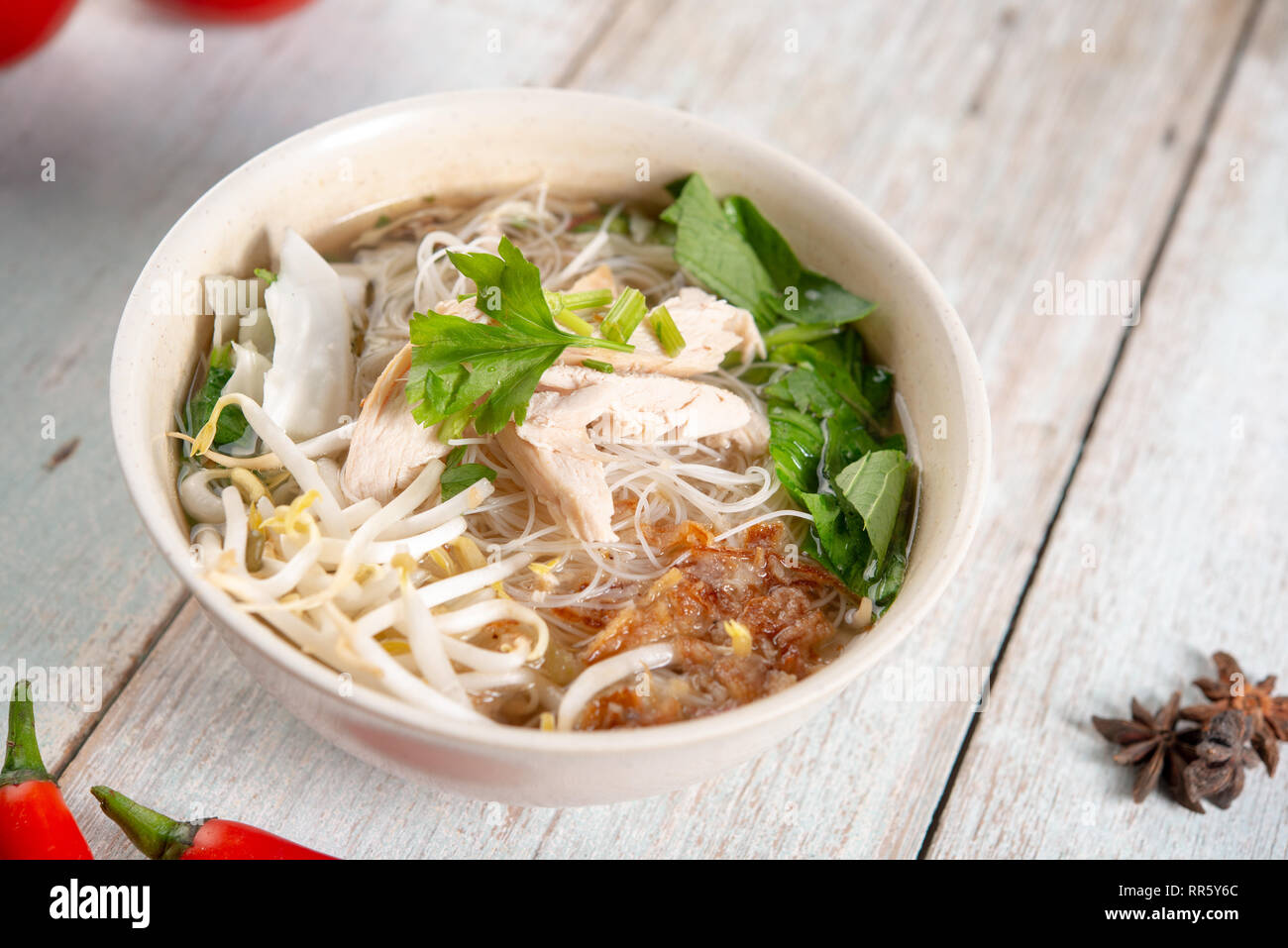 Asiatische Reisnudeln Suppe mit Gemüse und Huhn in Schüssel auf Holz- Hintergrund. Stockfoto