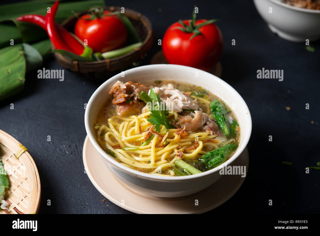 Asiatische Suppe, Nudeln und Huhn in Schüssel auf dunklem Hintergrund. Stockfoto