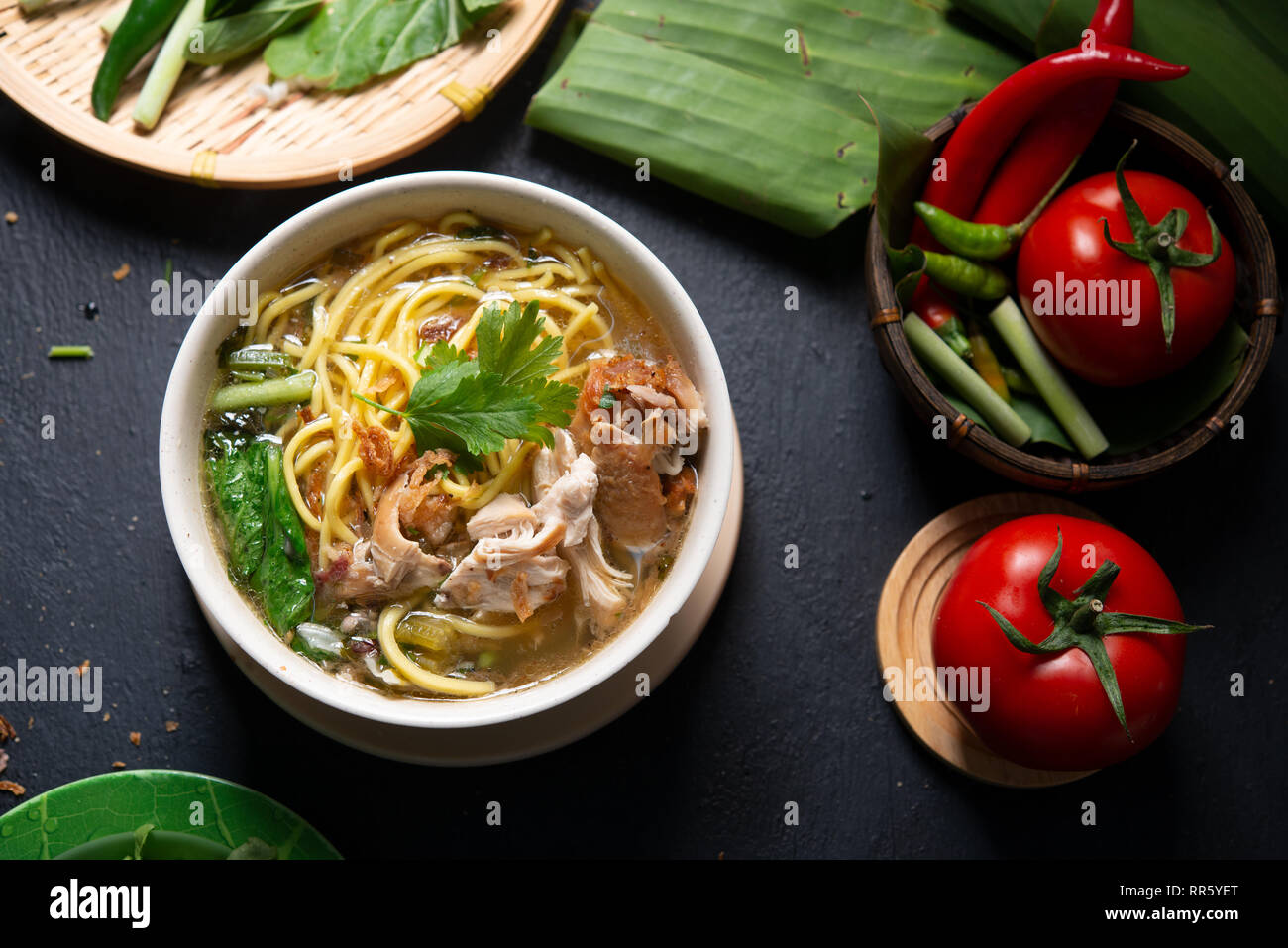 Asiatische Suppe, Nudeln und Huhn in Schüssel auf dunklem Hintergrund. Ansicht von oben flach. Stockfoto