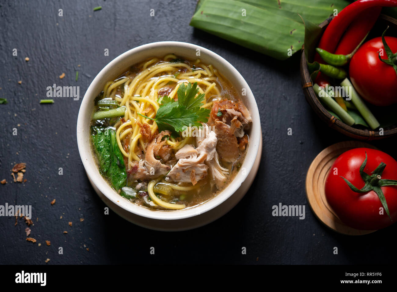 Asiatische Suppe, Nudeln und Huhn in Schüssel auf dunklem Hintergrund. Ansicht von oben flach. Stockfoto