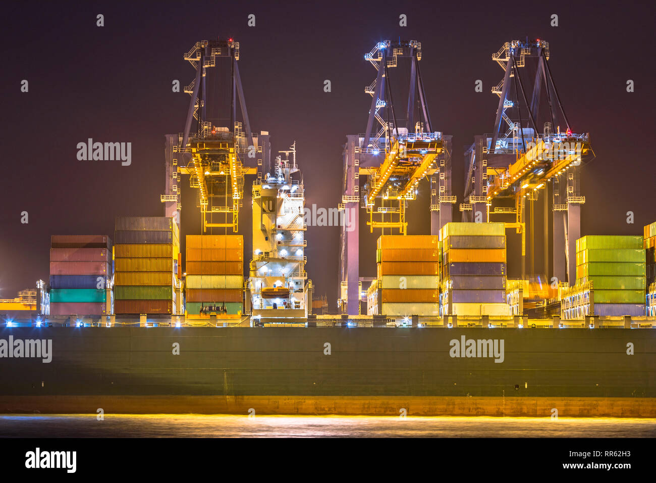 Beleuchtete Cargo Carrier Schiff in der Nacht in Rotterdam Maasvlakte Container Terminal in der Dunkelheit geladen. Die Niederlande Stockfoto