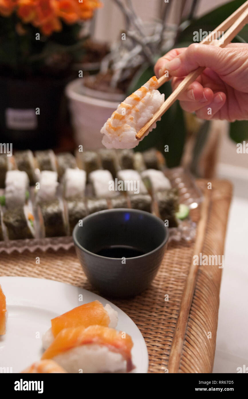 Nigiri Sushi mit Stäbchen von einer Frau in einem Haus im Hintergrund gehalten Stockfoto