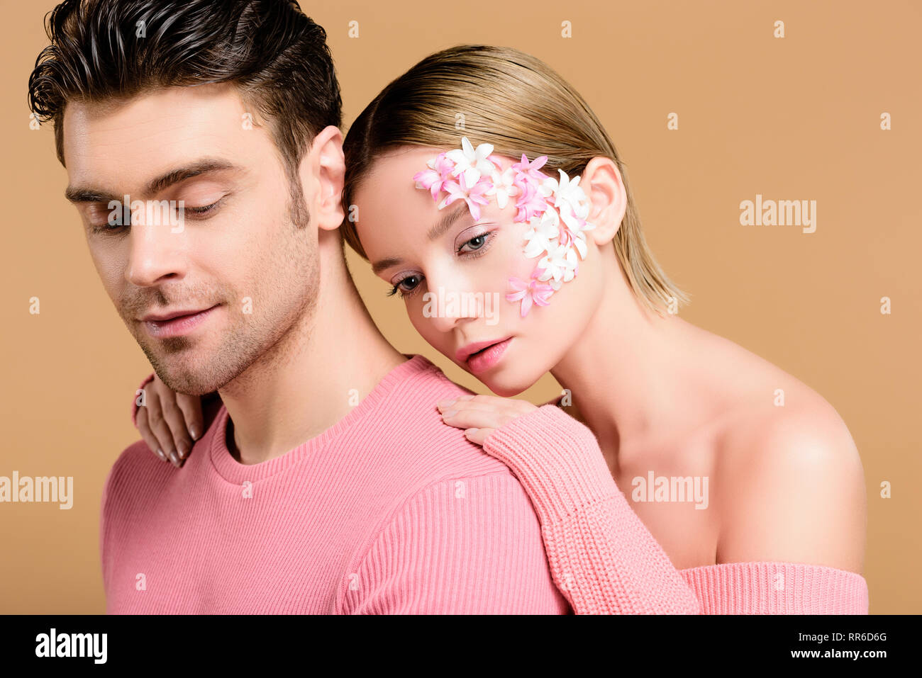 Attraktive Frau mit Blumen auf dem Gesicht umarmen Mann isoliert auf beige Stockfoto Attraktive Frau mit Blumen auf dem Gesicht umarmen Mann isoliert auf beige Stockfoto