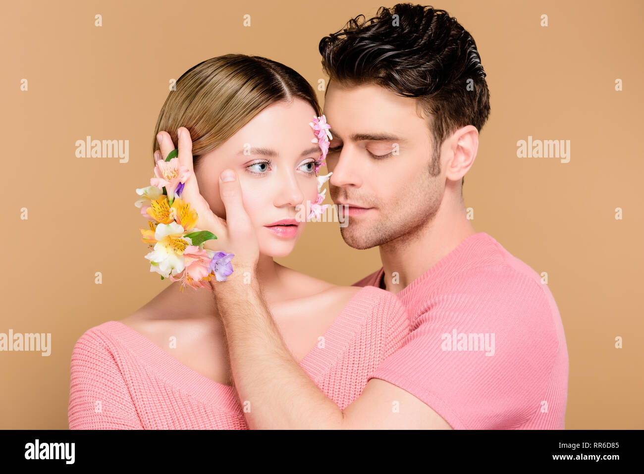 Schöner Mann berühren Gesicht der Freundin mit Blumen auf dem Gesicht isoliert auf beige Stockfoto Schöner Mann berühren Gesicht der Freundin mit Blumen auf dem Gesicht isoliert auf beige Stockfoto