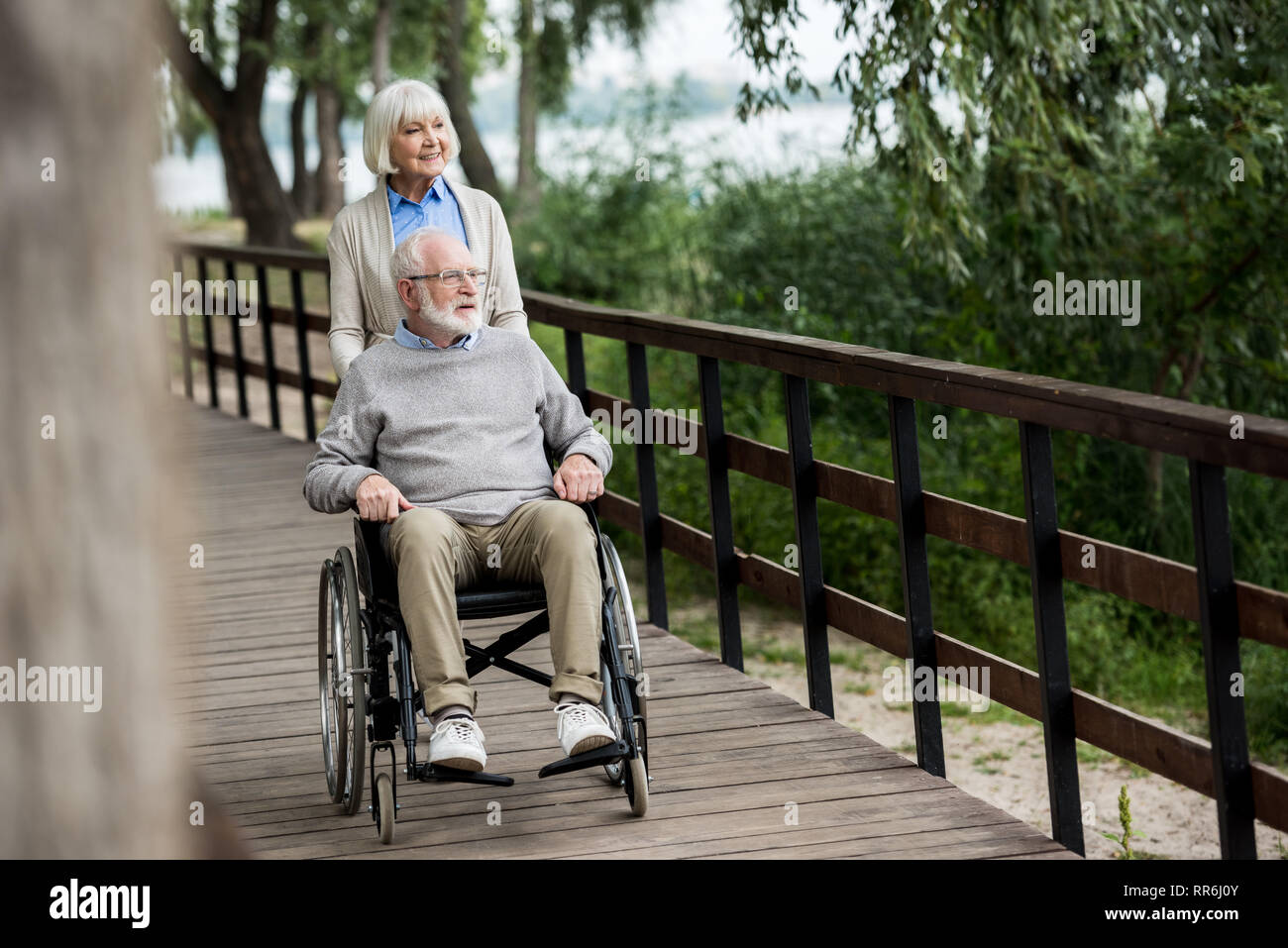 Lächelnde ältere Frau mit Mann im Rollstuhl beim Spaziergang im Park Stockfoto
