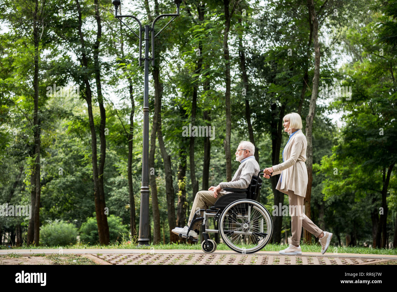 Ältere Frau, die Mann im Rollstuhl beim Spaziergang im Park Stockfoto