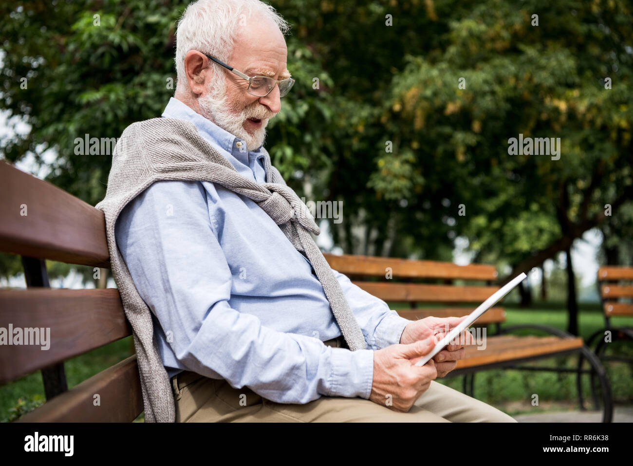 Selektiver Fokus der ältere Mann mit digitalen Tablet während auf Holzbank im Park sitzen Stockfoto