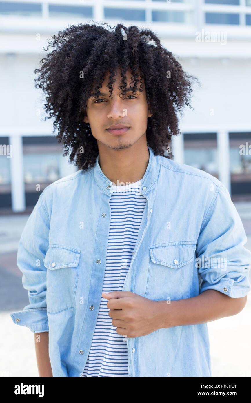Lateinamerikanischen junger erwachsener Mann mit Langen lockigen Haar im Freien in der Stadt Stockfoto