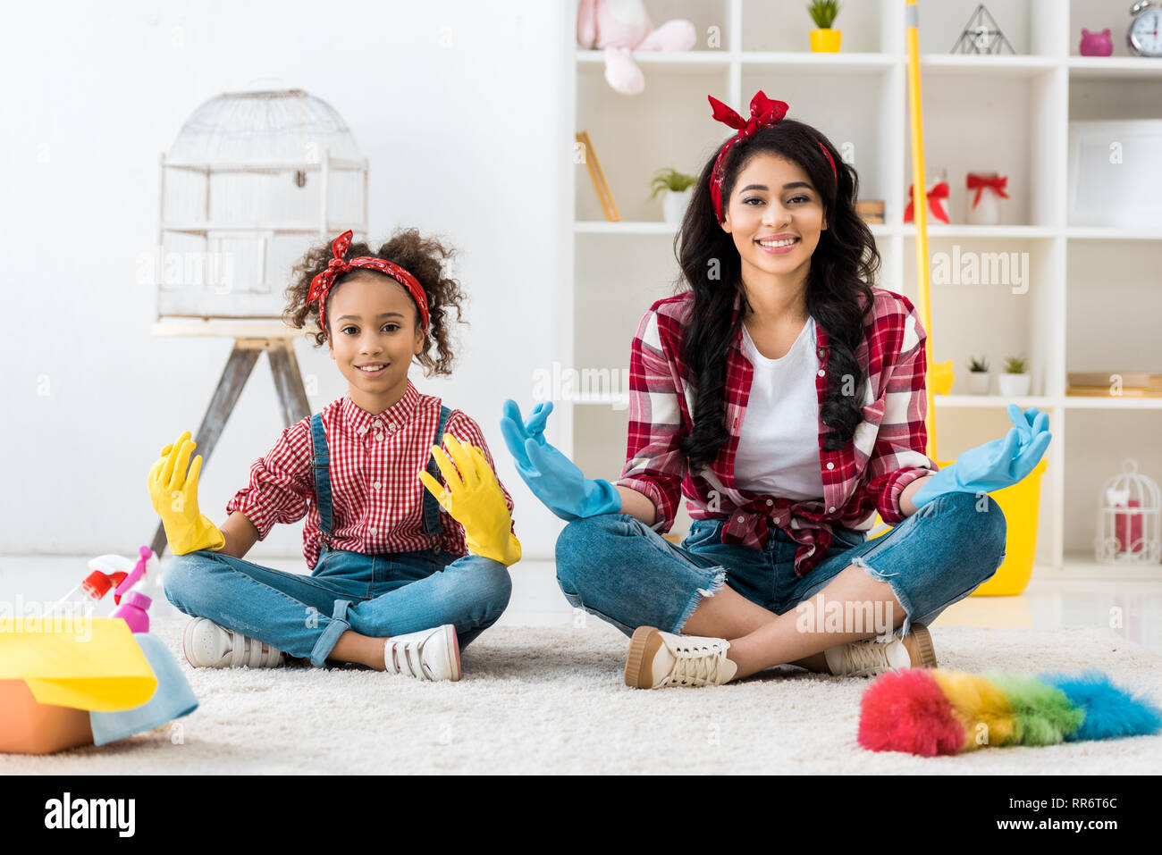 Lächelnd afrikanischen amerikanischen Mutter und Tochter und karierte Hemden und hellen Gummihandschuhe im Lotussitz sitzen Stockfoto