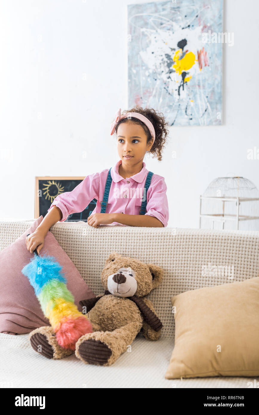 Cute afrikanische amerikanische Kind abstauben Sofa mit Kissen und Teddybär Stockfoto