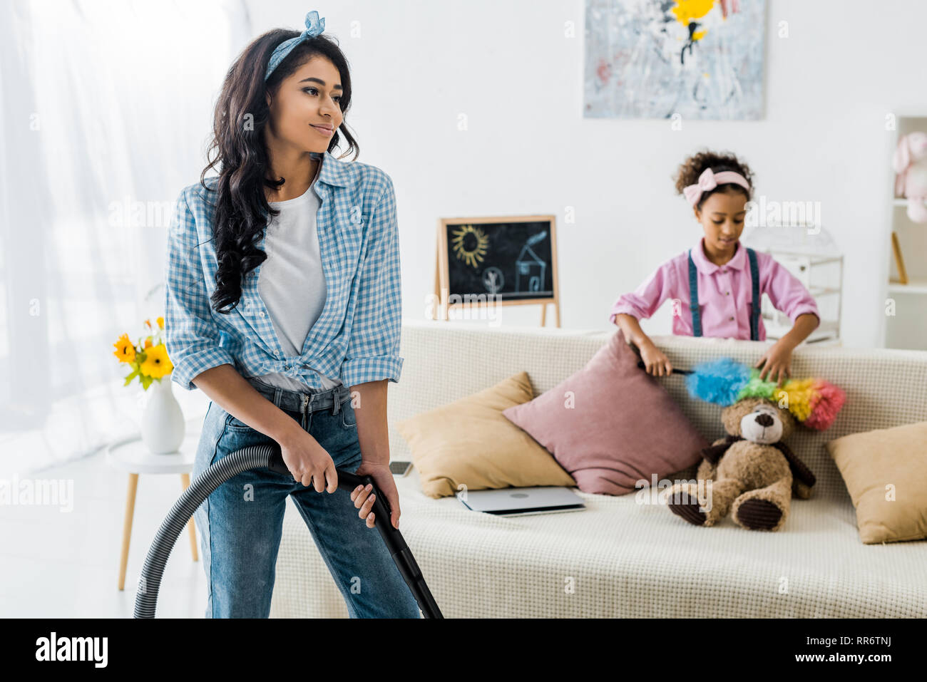 Selektiver Fokus Staubsaugen afrikanische amerikanische Frau und niedlichen Tochter abstauben Teddybär Stockfoto