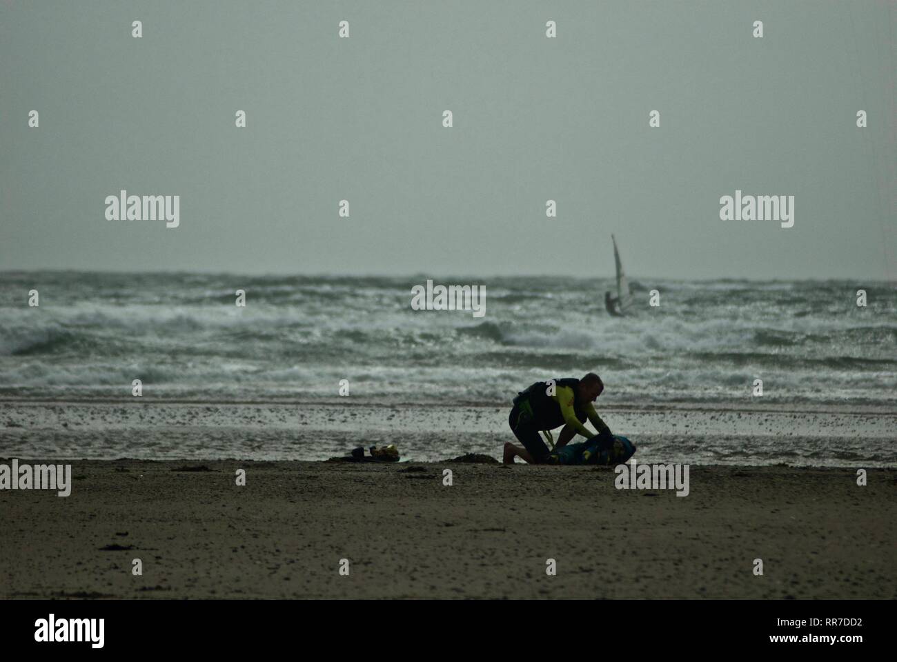 Windsurfer Segel auf dramatische White Water in grauen bewölkten Wetter in Rhosneigr, Anglesey, North Wales, UK Stockfoto