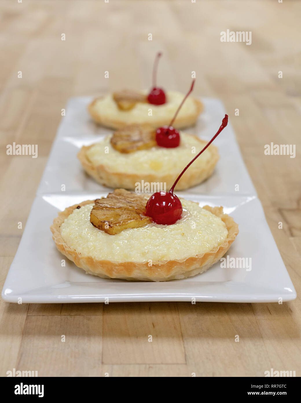 Drei Pudding in einer Reihe auf weiße quadratische Platten. Mit glasierten Ananas und Kirschen garniert. Holz- Hintergrund. Stockfoto