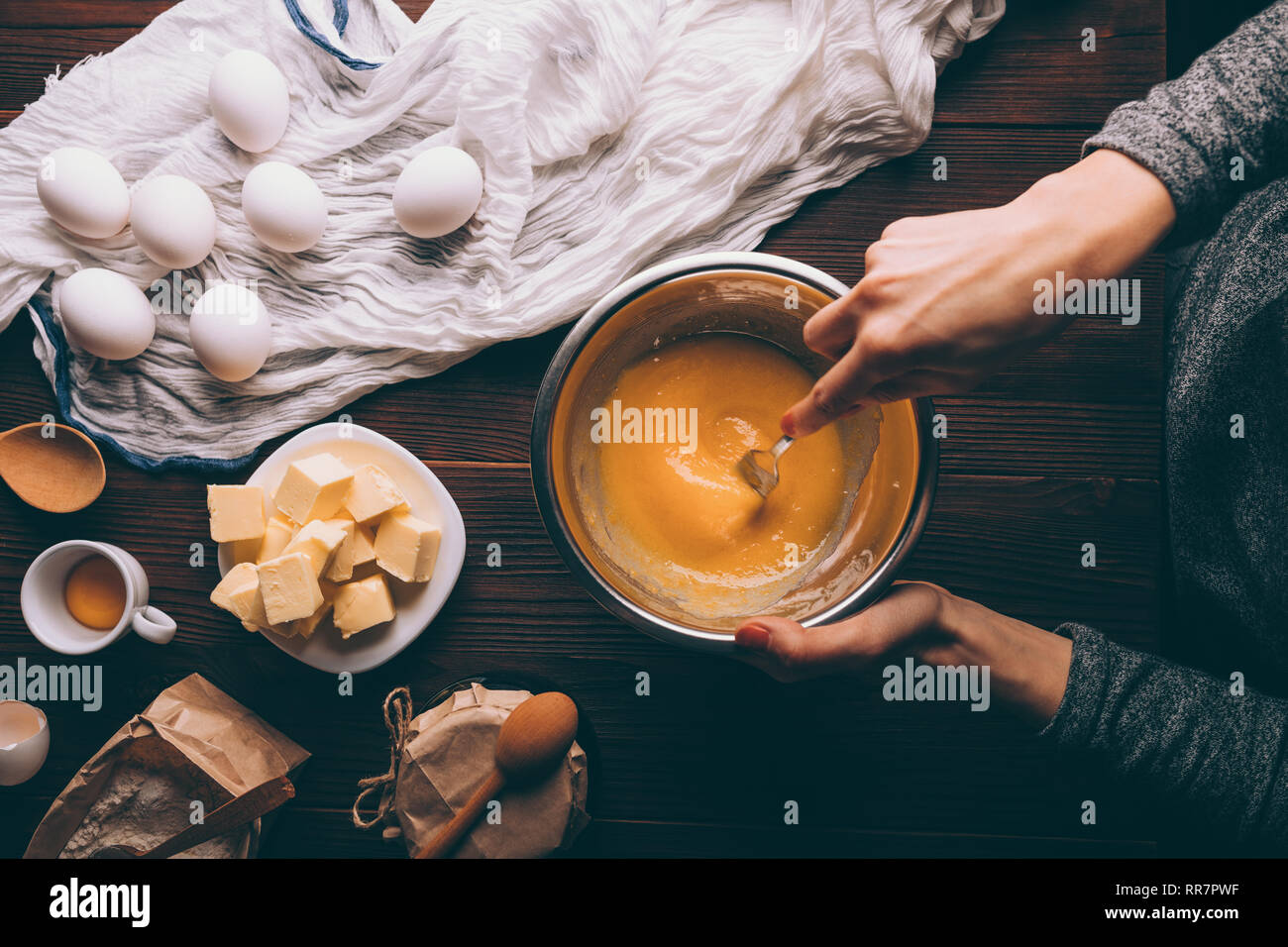 Die Ansicht von Oben weibliche Hände rühren, Zucker und Eigelb in Metall  Schüssel weiter Butter, Mehl und Eiern auf braunem Holz- Küche Tabelle  gewürfelt. Prozess des Kochens Stockfotografie - Alamy