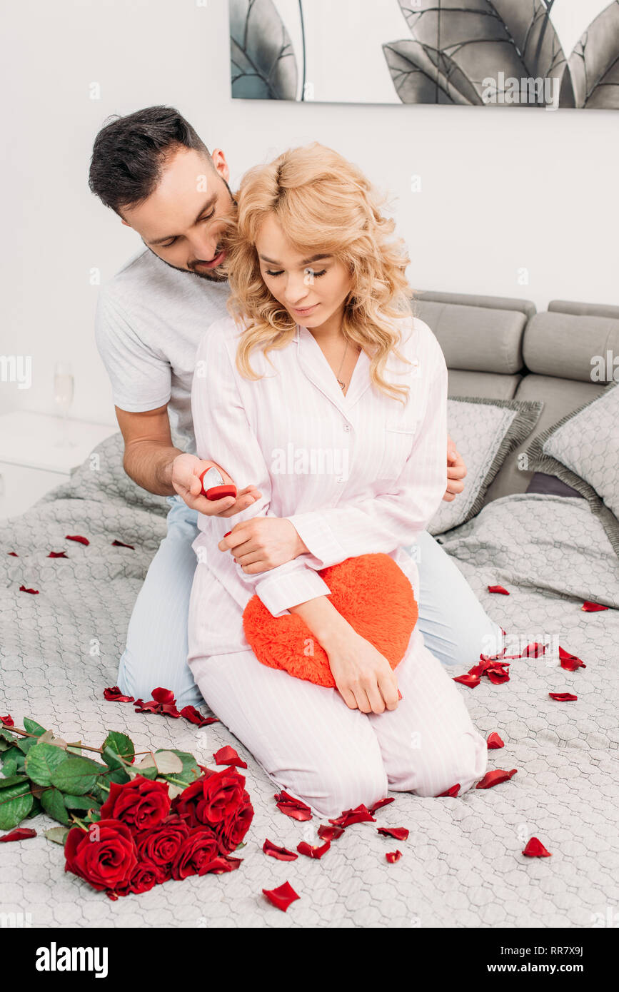 Schöner Mann sitzen auf dem Bett mit Rosen und vorschlägt, attraktive Frau Stockfoto