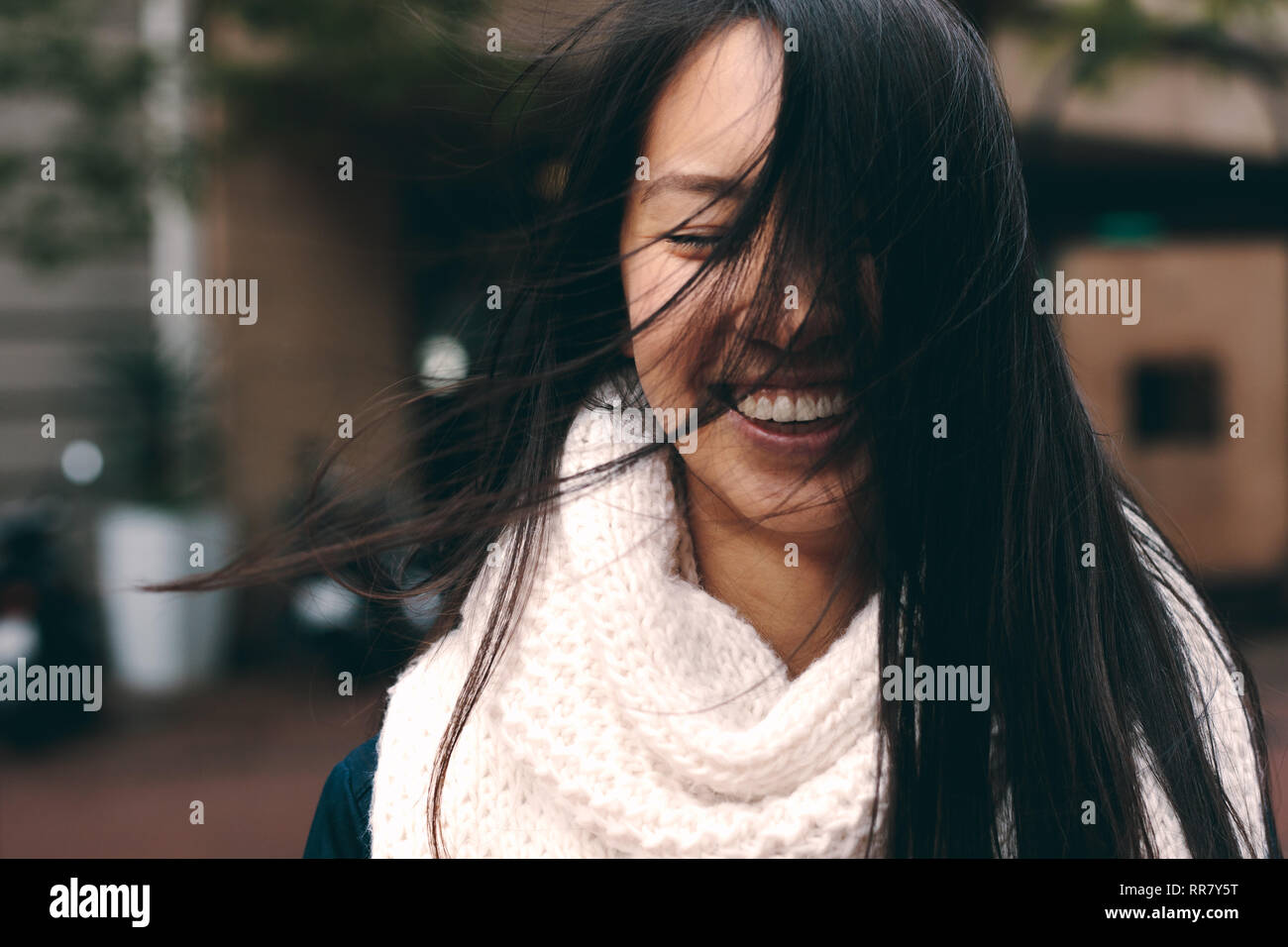 Lächelnde Frau auf der Straße mit Haare fliegen im Gesicht. Nahaufnahme  einer asiatischen Frau in Winterkleidung stehen draußen mit ihr Haar  bedecken Ihre f Stockfotografie - Alamy