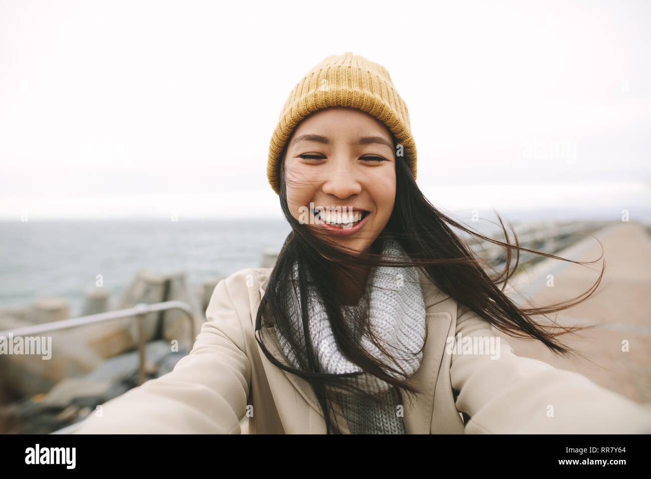 Nahaufnahme von einem lächelnden Frau im Winter tragen, stehen in der Nähe des Meeres. Asiatische Frau, die draußen an einem kalten Wintermorgen mit offenen Armen. Stockfoto